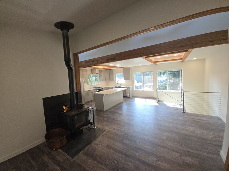 Open-concept living room with a lit wood-burning stove looking through to the kitchen