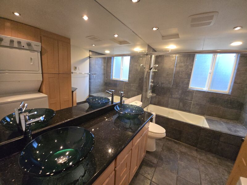 Lower-level bathroom with dual glass vessel sinks, granite counter, jetted tub, and in-unit washer and dryer